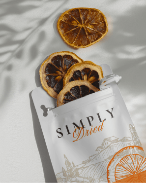 A white resealable bag labeled "Simply Dried" lies on a flat surface, with three dried orange slices partially spilling out. One additional dried orange slice rests beside the bag. Soft shadows of leaves are visible on the surface, adding a natural touch, showcasing thoughtful package design in the food industry.